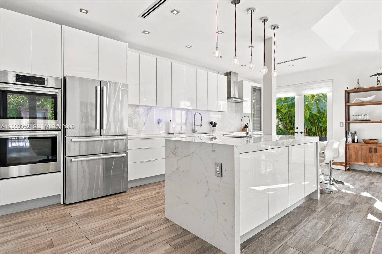 1516 Breakwater Terrace, Hollywood, FL 33019 Modern kitchen featuring high-gloss white cabinetry, a center island with a stone-finish waterfall countertop, stainless steel double wall ovens, wood-finish flooring, and pendant lighting