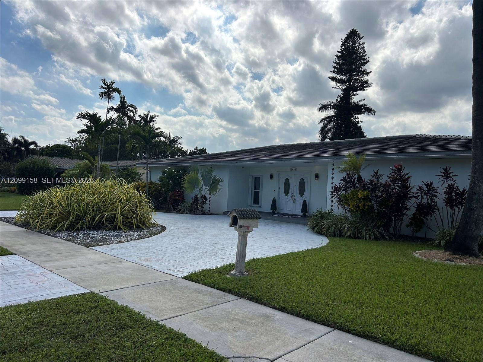 1490 Lenape Drive, Miami Springs, FL 33166 Waterfront lot featuring a grass lawn, mature palm tree, and bulkhead retaining wall