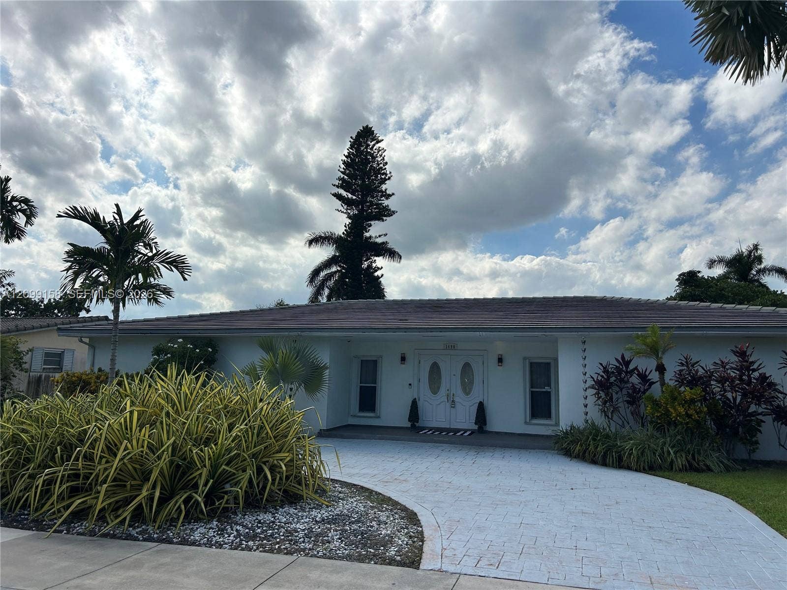 1490 Lenape Drive, Miami Springs, FL 33166 Single-story residence featuring a paved circular driveway, double-door entry with oval glass inserts, and lush professional landscaping