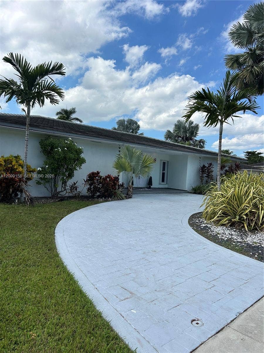 1490 Lenape Drive, Miami Springs, FL 33166 Single-story exterior featuring a tile roof, paved circular driveway, double-door entry with glass inserts, and established tropical landscaping