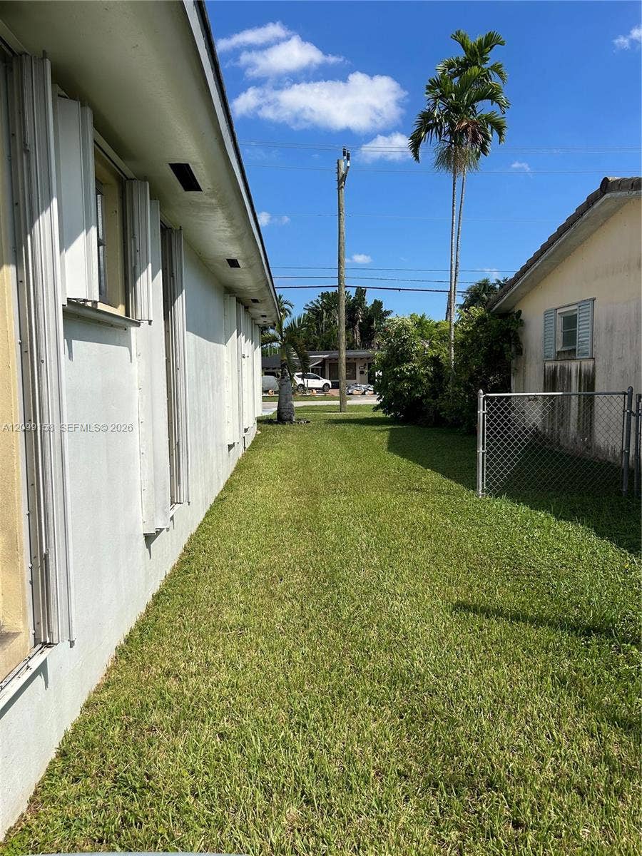 1490 Lenape Drive, Miami Springs, FL 33166 Exterior side yard featuring a grass lawn, chain-link fencing, and mature palm trees