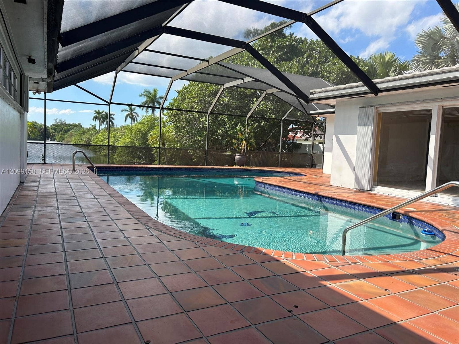 1490 Lenape Drive, Miami Springs, FL 33166 Screen-enclosed pool area featuring ceramic tile decking, built-in metal pool ladder, and multiple sets of sliding glass doors