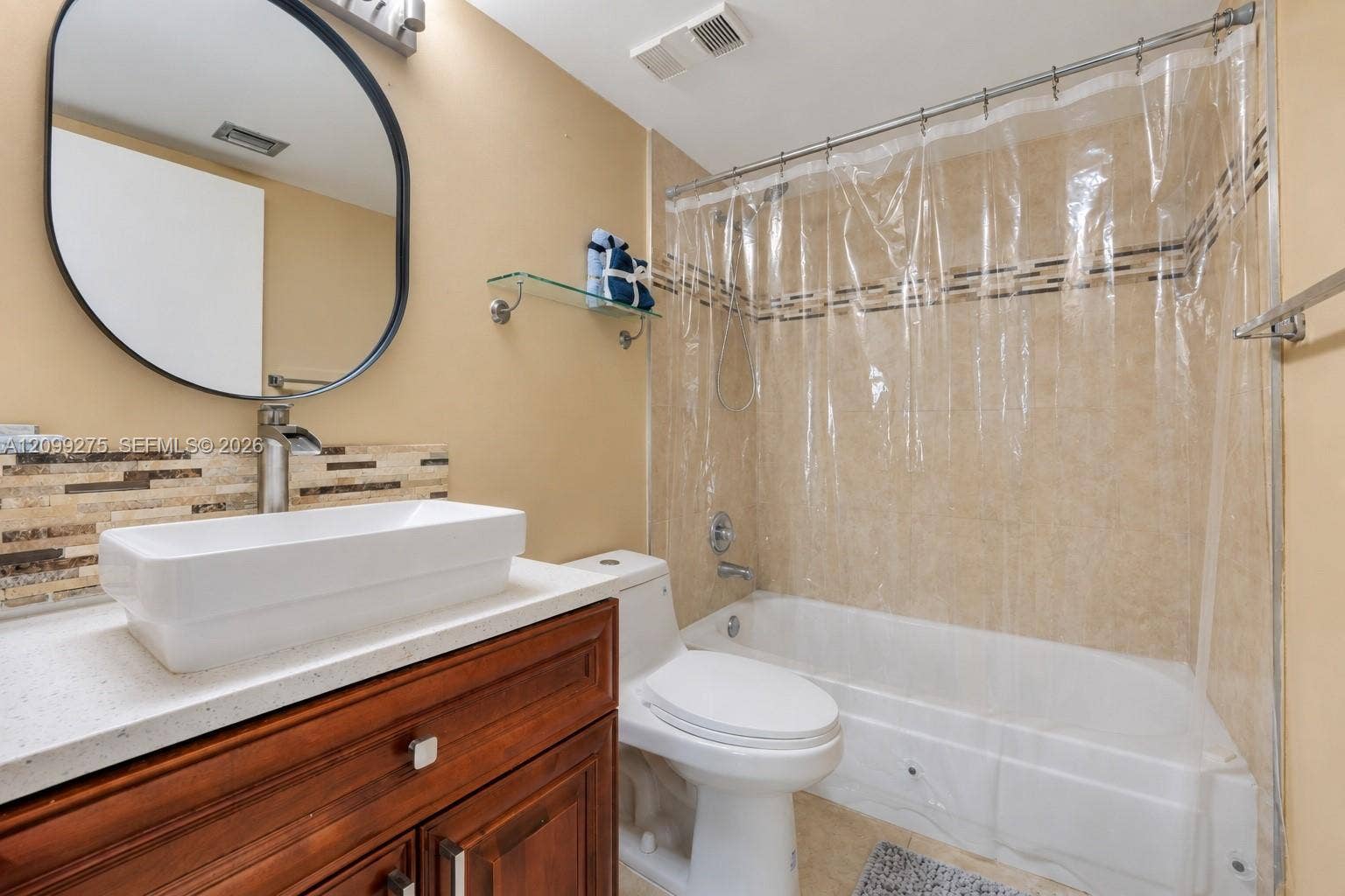 800 N Miami Avenue, #E-902, Miami, Miami, FL 33136 Spacious bathroom featuring a white bathtub with tiled surround, modern vessel sink, rich wood vanity, round mirror, and glass display shelves.