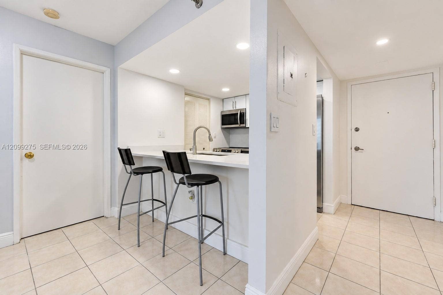 800 N Miami Avenue, #E-902, Miami, Miami, FL 33136 Bright, modern kitchen featuring a sleek breakfast bar with contemporary seating, recessed lighting, and elegant tile flooring, offering a clean and inviting space.