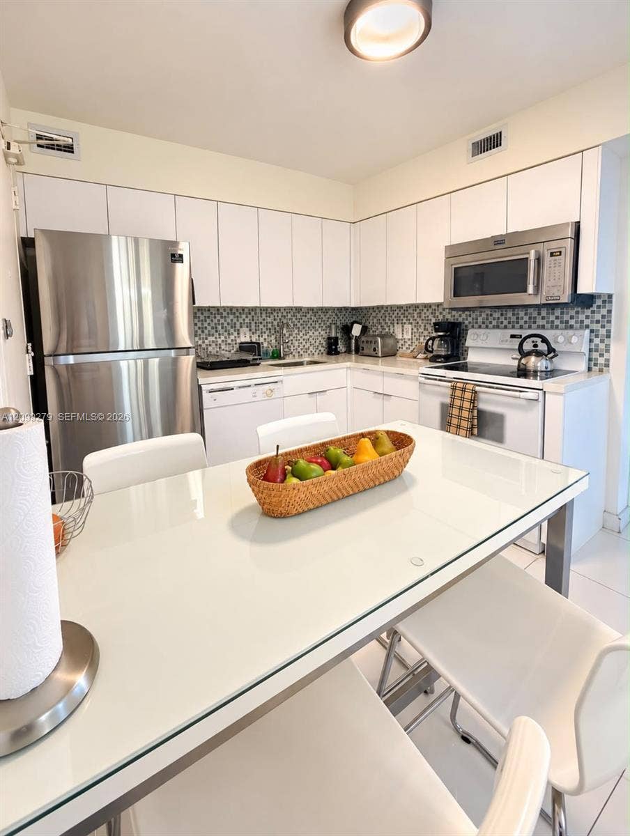 5151 Collins Avenue, #921, Miami Beach, Miami Beach, FL 33140 Kitchen featuring white cabinetry, stainless steel appliances, a mosaic tile backsplash, and light-toned tile flooring