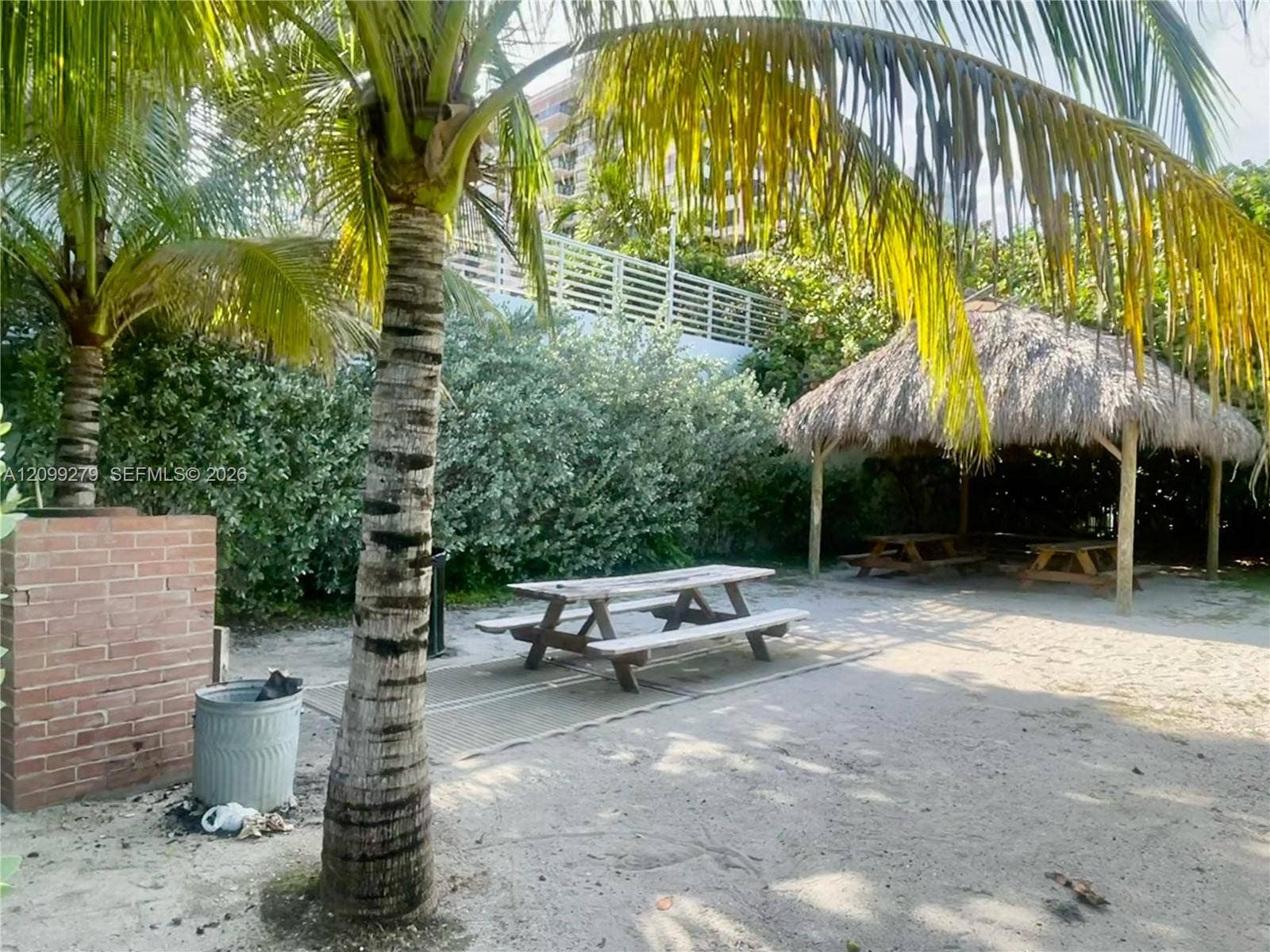 5151 Collins Avenue, #921, Miami Beach, Miami Beach, FL 33140 Outdoor common area featuring a thatched-roof tiki hut, sandy grounds, brick masonry structure, and mature palm trees