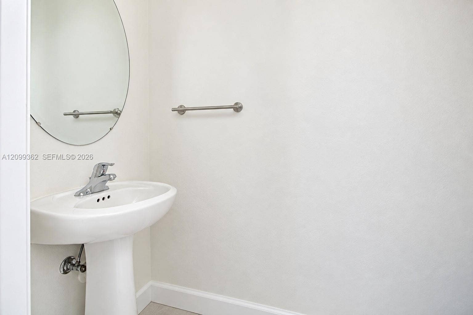 16230 SW 290th Terrace, Homestead, FL 33033 White pedestal sink with a polished chrome faucet, oval frameless wall mirror, and polished chrome towel bar
