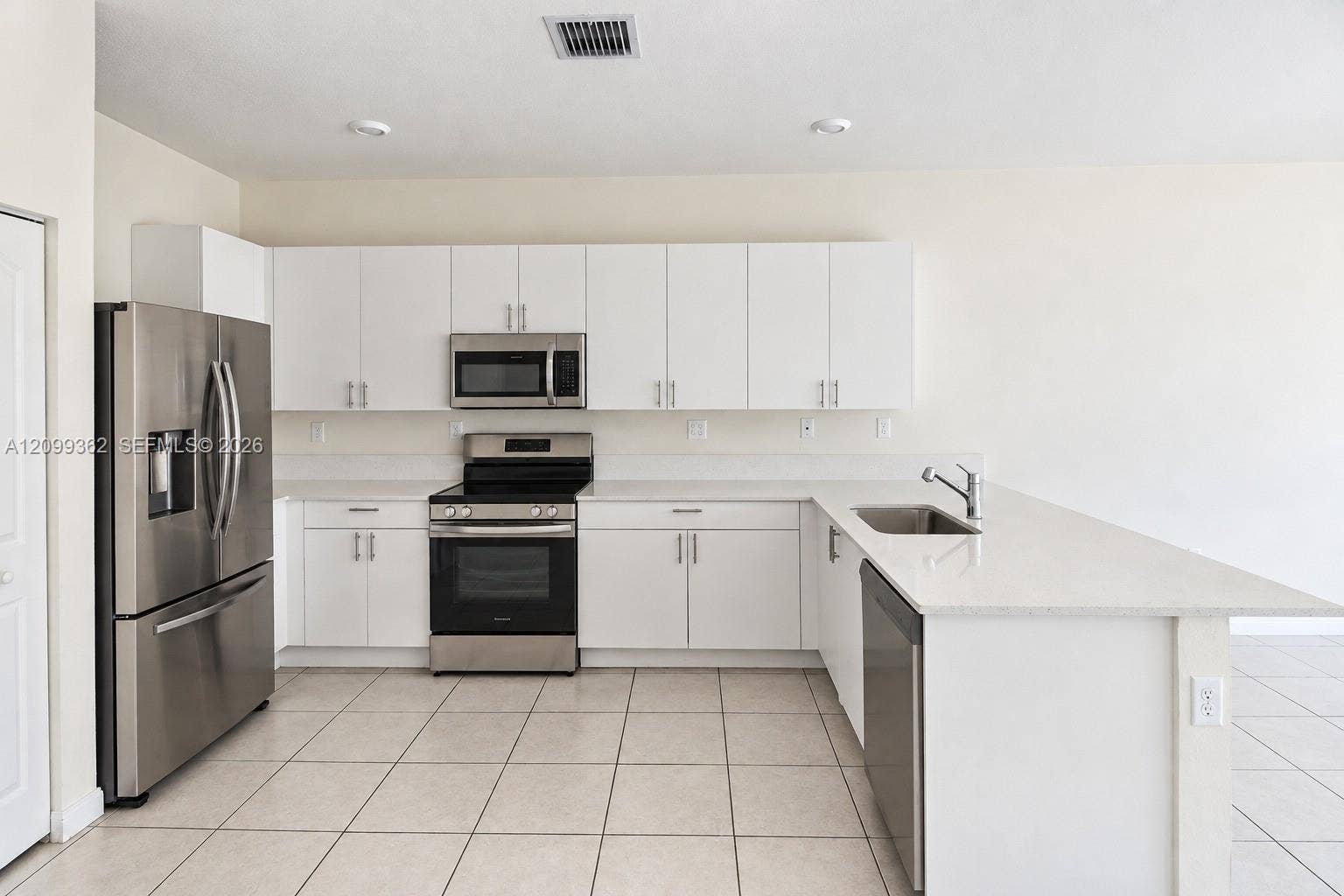 16230 SW 290th Terrace, Homestead, FL 33033 Kitchen featuring white shaker-style cabinetry, solid-surface countertops, stainless steel appliances, a peninsula with an undermount sink, and tiled flooring