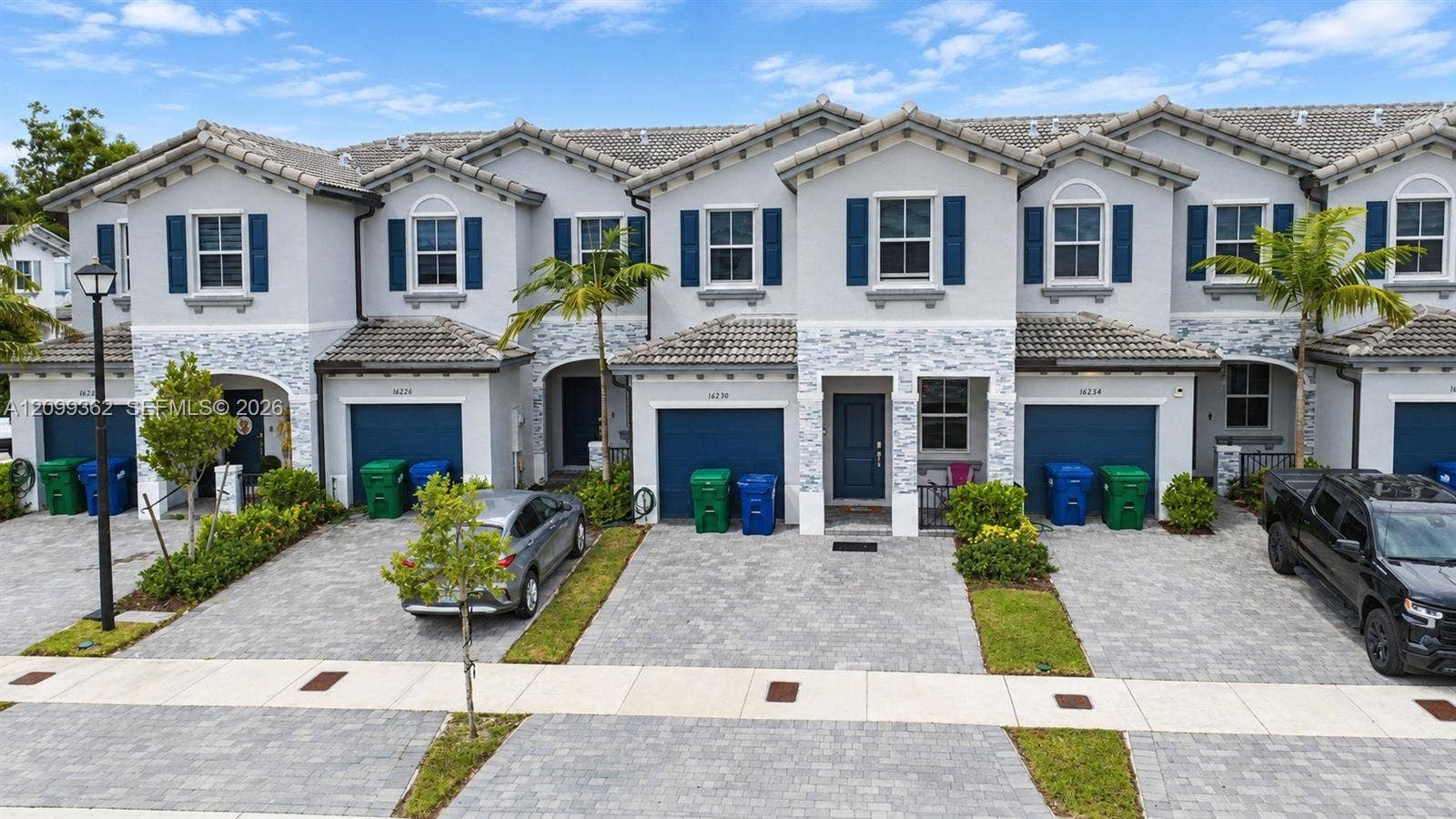 16230 SW 290th Terrace, Homestead, FL 33033 Two-story townhome exterior featuring stucco siding, stone veneer accents, multi-pane windows with decorative shutters, tile roofing, and paver driveways