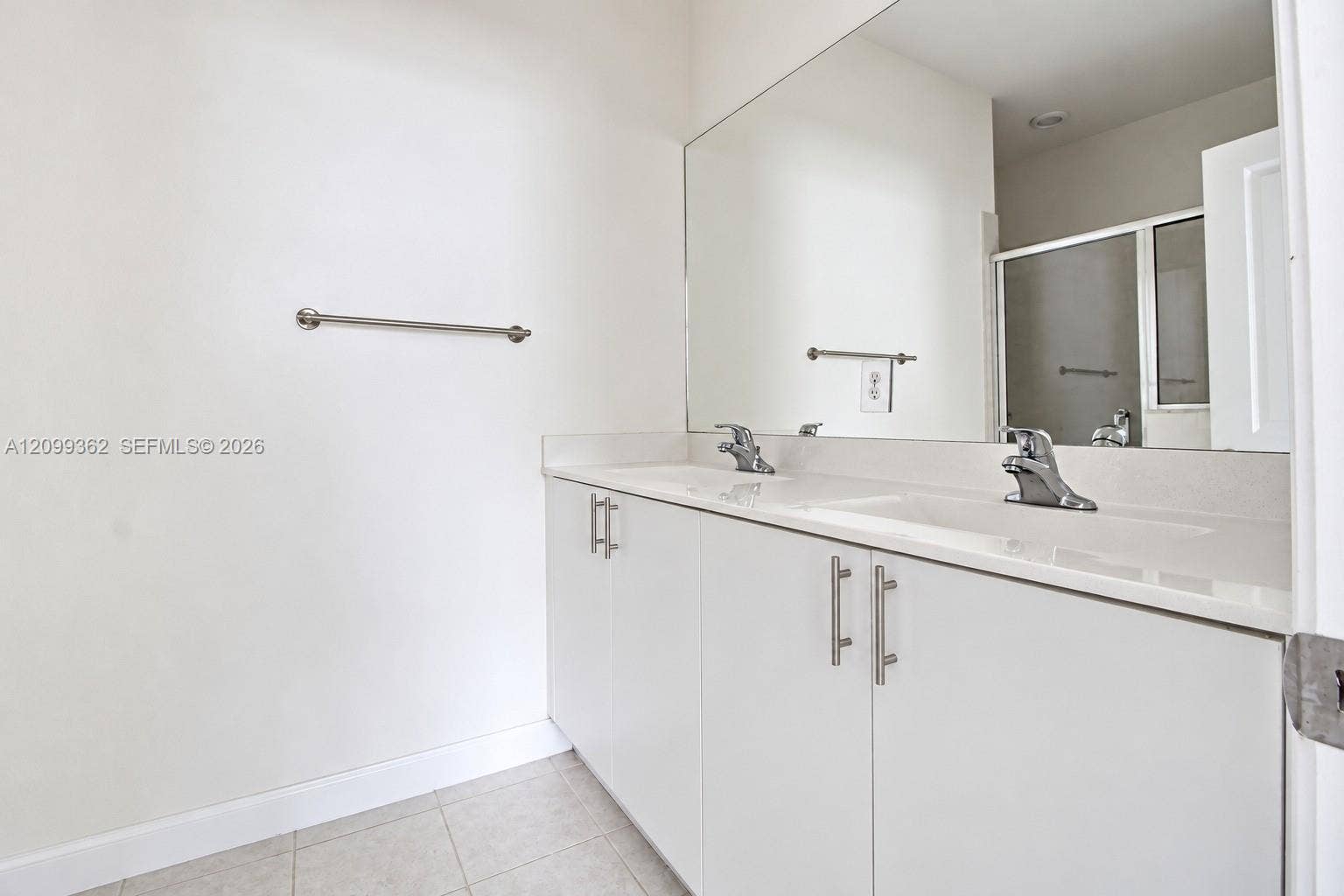 16230 SW 290th Terrace, Homestead, FL 33033 Dual-sink vanity with a solid-surface countertop, cabinetry featuring stainless steel pulls, an expansive wall-mounted mirror, and tile flooring