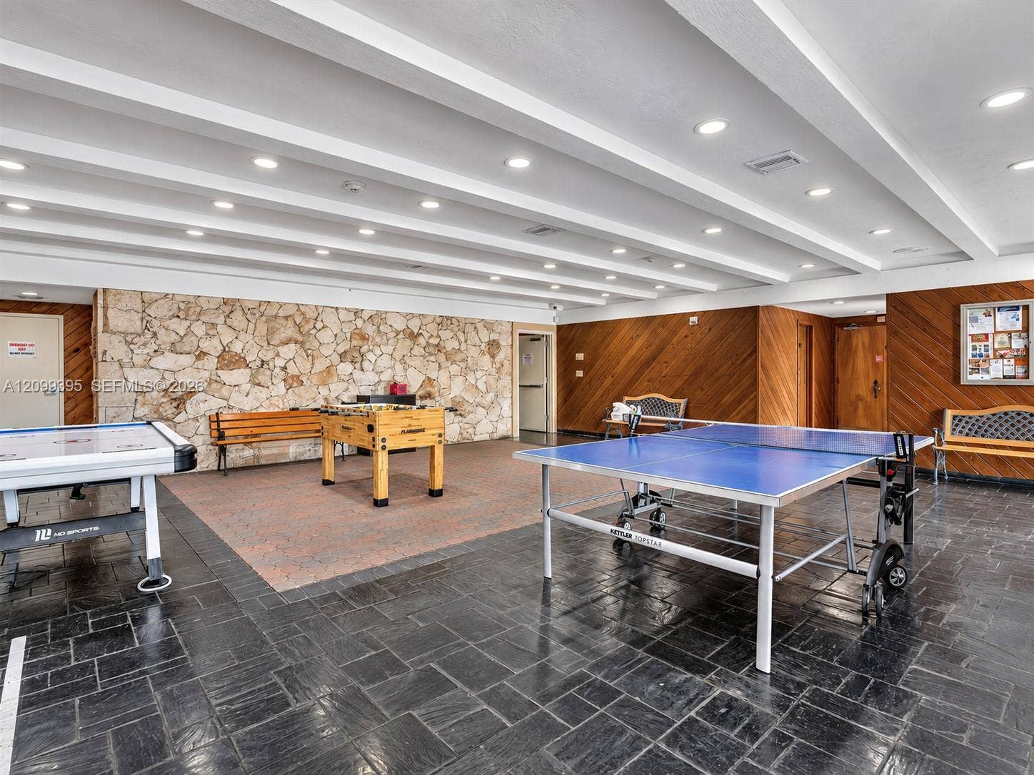 Textured natural stone accent wall, wood-paneled wall detailing, dark slate tile flooring, and recessed ceiling lighting with exposed beam accents
