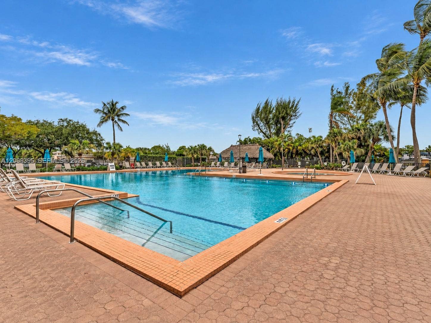 In-ground swimming pool with a tile-bordered edge, stainless steel entry handrails, and a paved brick pool deck