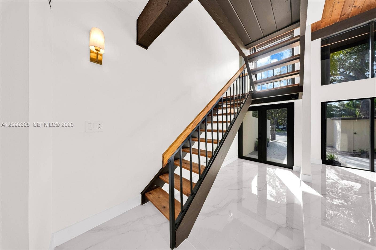 Staircase featuring open wood treads, black metal railings, and a wood handrail, polished white tile flooring, exposed dark wood ceiling beams, and floor-to-ceiling glass paneling
