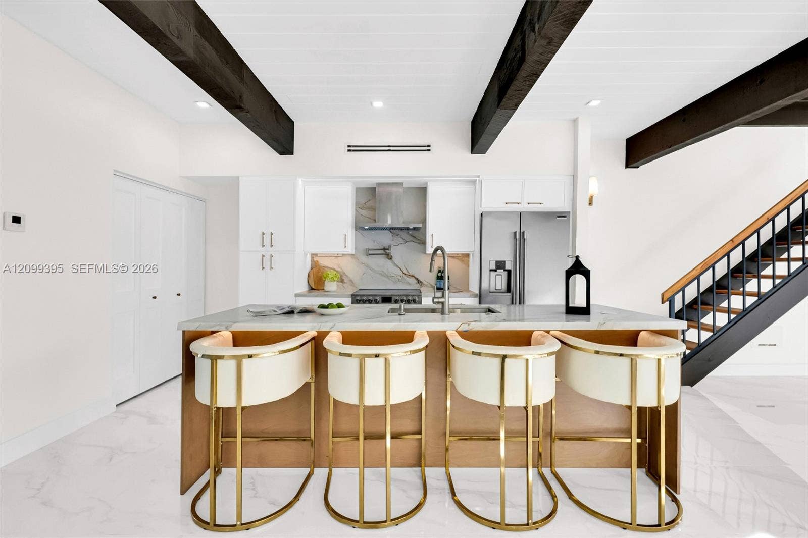 Kitchen featuring dark cedar wood-finish ceiling beams, white slim shaker-style cabinetry, stone-finish countertops, stainless steel appliances, and large-format tile flooring
