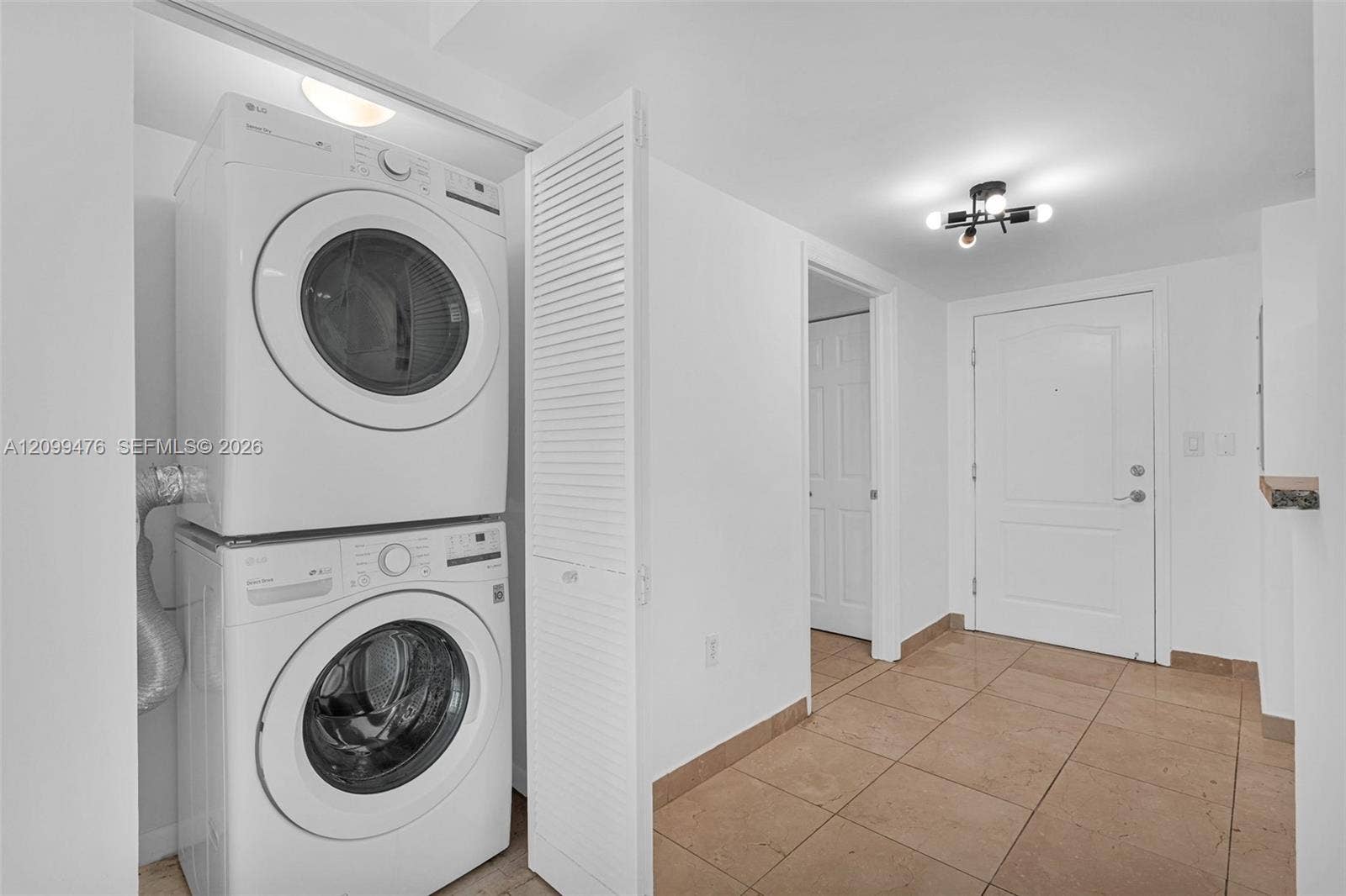 Stacked laundry center with white louvered door, tile flooring, and multi-light flush mount ceiling fixture