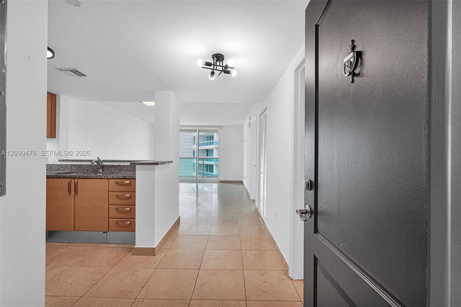 Entryway featuring a dark solid-panel door, tile flooring, kitchen with stone countertops and wood-finish cabinetry, and glass sliding doors