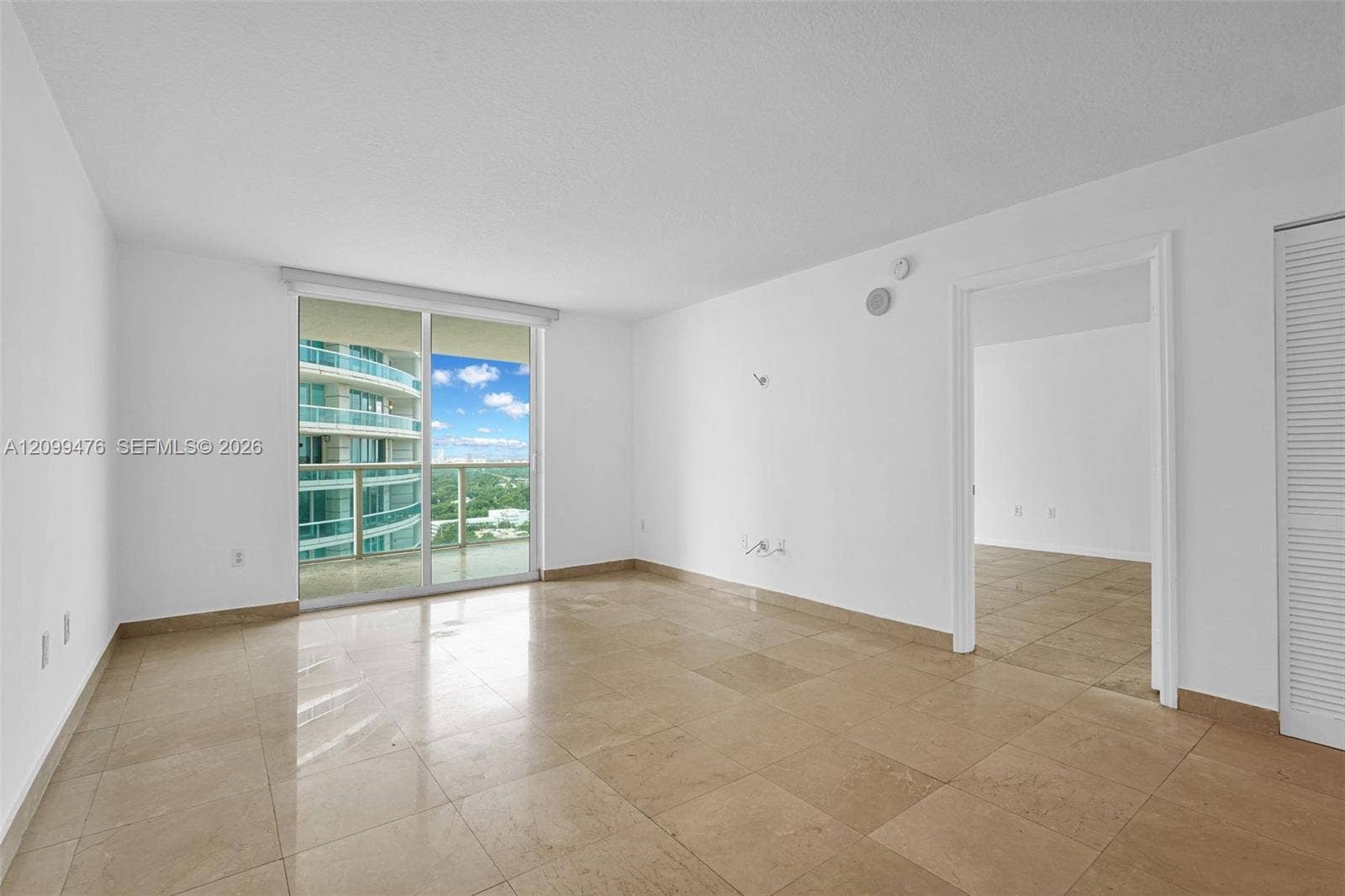Neutral-toned tile flooring, large sliding glass door, private balcony, and louvered closet door