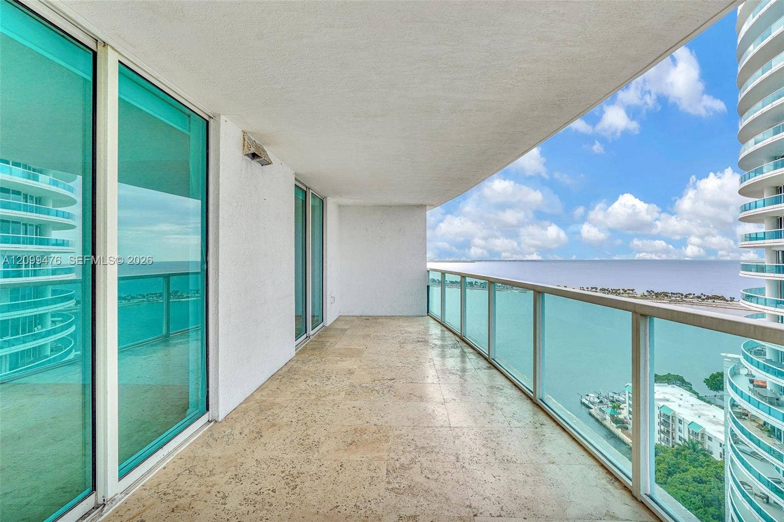 Covered balcony featuring stone tile flooring and a glass panel railing overlooking water