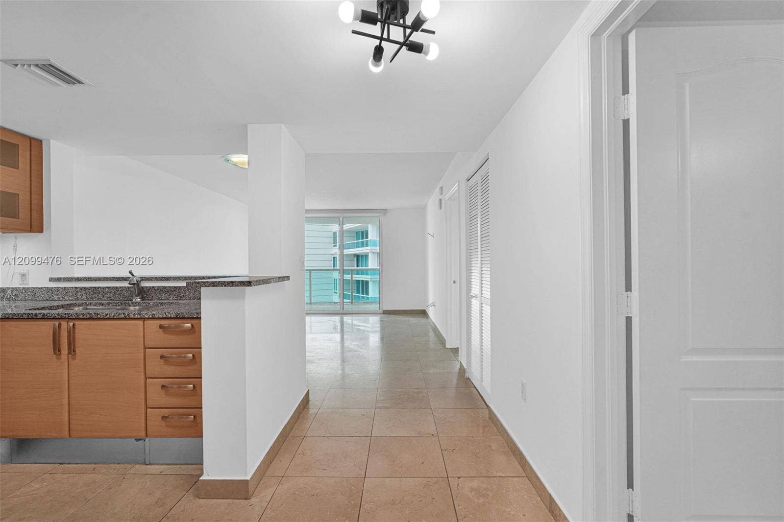 Kitchen featuring wood-finish cabinetry, stone-surfaced countertops, neutral tile flooring, louvered closet doors, and a multi-bulb geometric light fixture