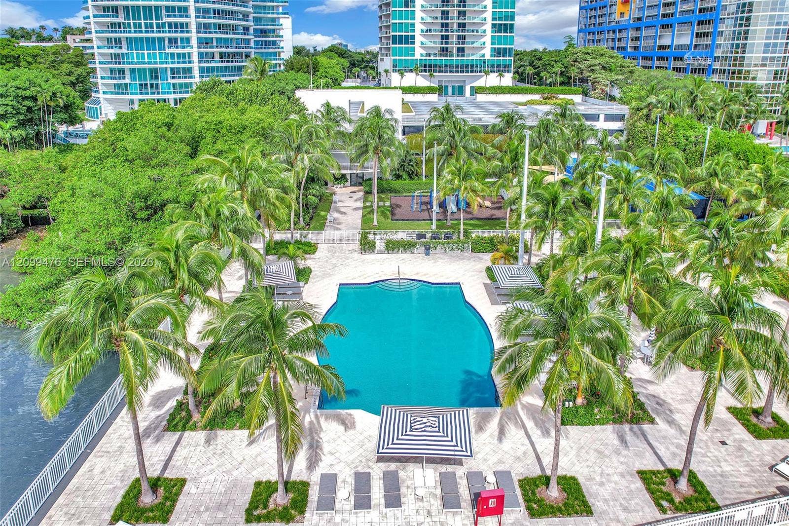 Swimming pool with stone-paved deck, mature palm trees, perimeter fencing, and integrated outdoor recreational area