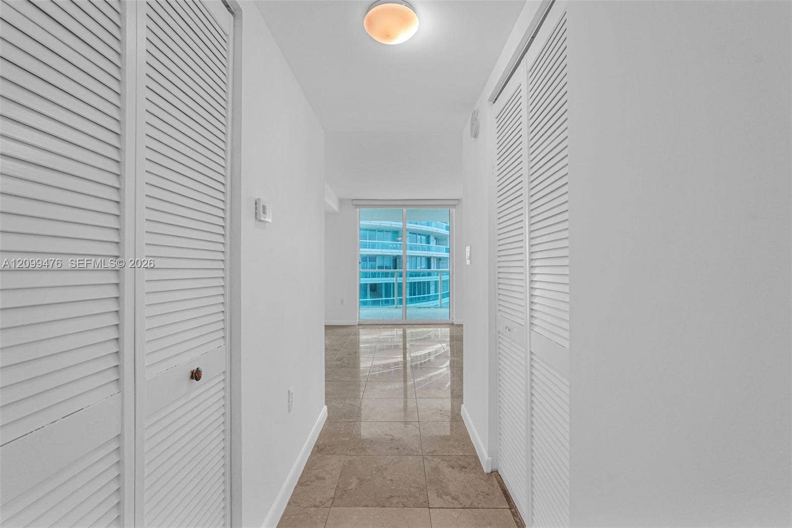 Hallway featuring polished tile flooring, dual floor-to-ceiling closets with white louvered doors, and a flush-mount dome light fixture