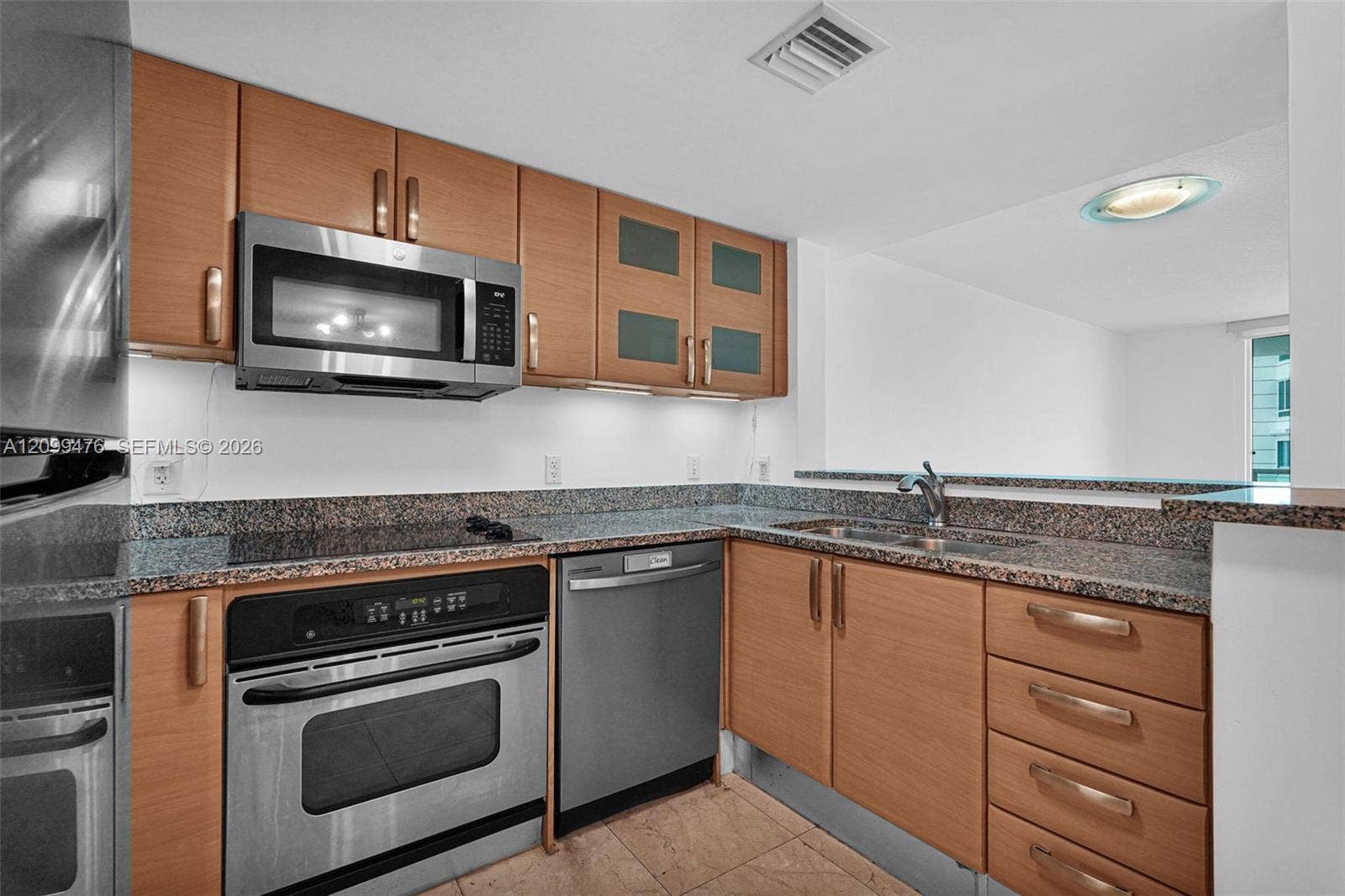 Kitchen featuring wood-finish cabinetry, stainless steel appliances, stone-surface countertops, and tiled flooring
