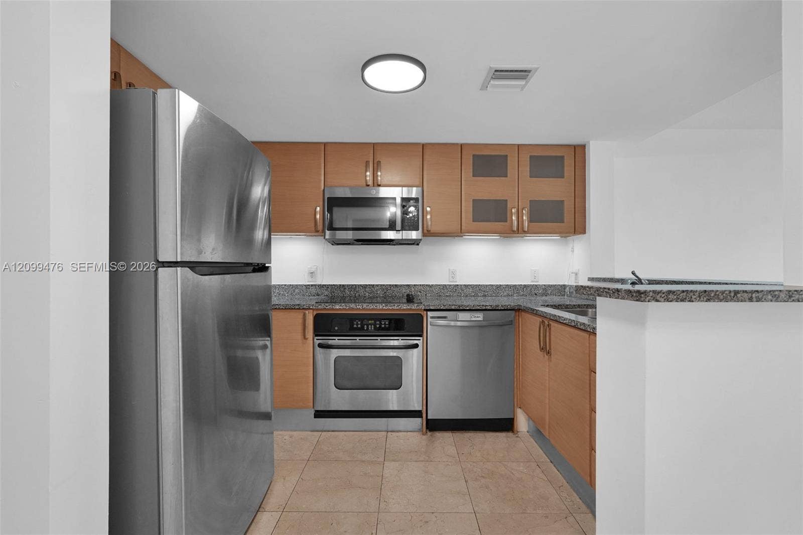 Kitchen featuring flat-panel wood cabinetry, speckled stone countertops, stainless steel appliances, and tile flooring
