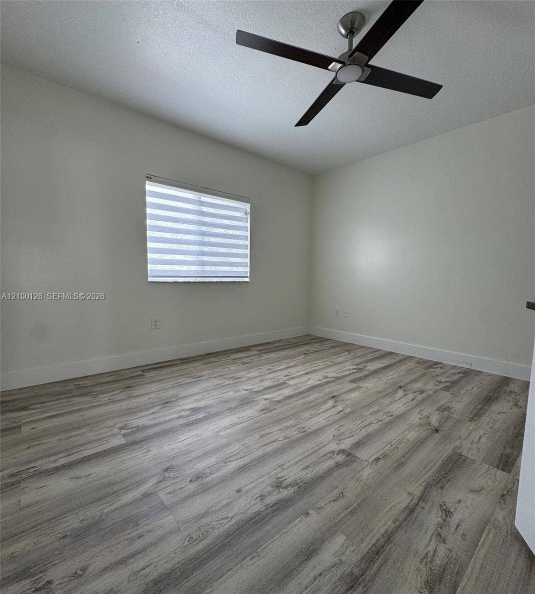 Interior space featuring wood-finish flooring, neutral walls, a modern ceiling fan with integrated lighting, and a window equipped with horizontal roller shades