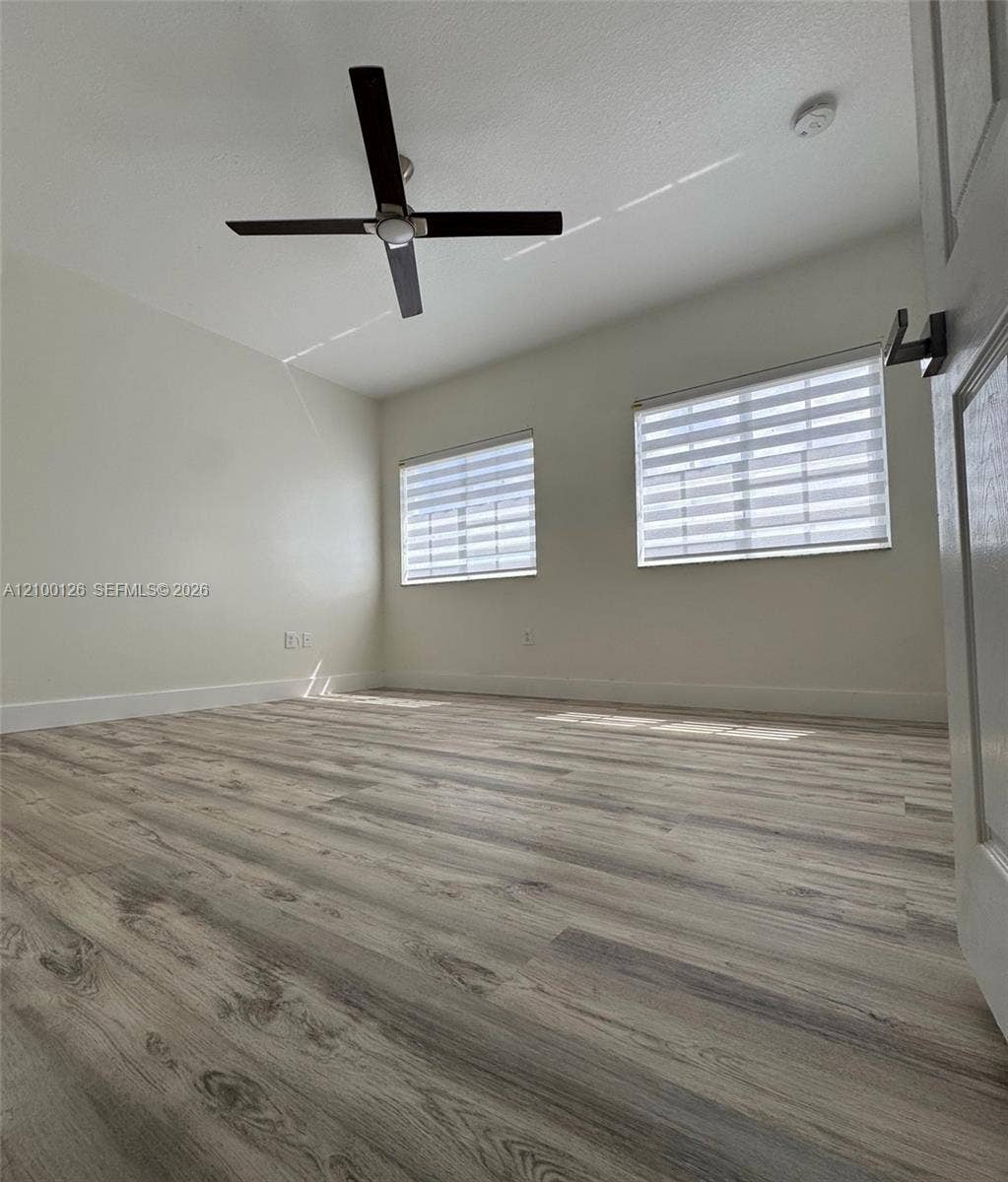 Interior room featuring wood-finish flooring, a four-blade ceiling fan, and dual windows equipped with horizontal privacy blinds