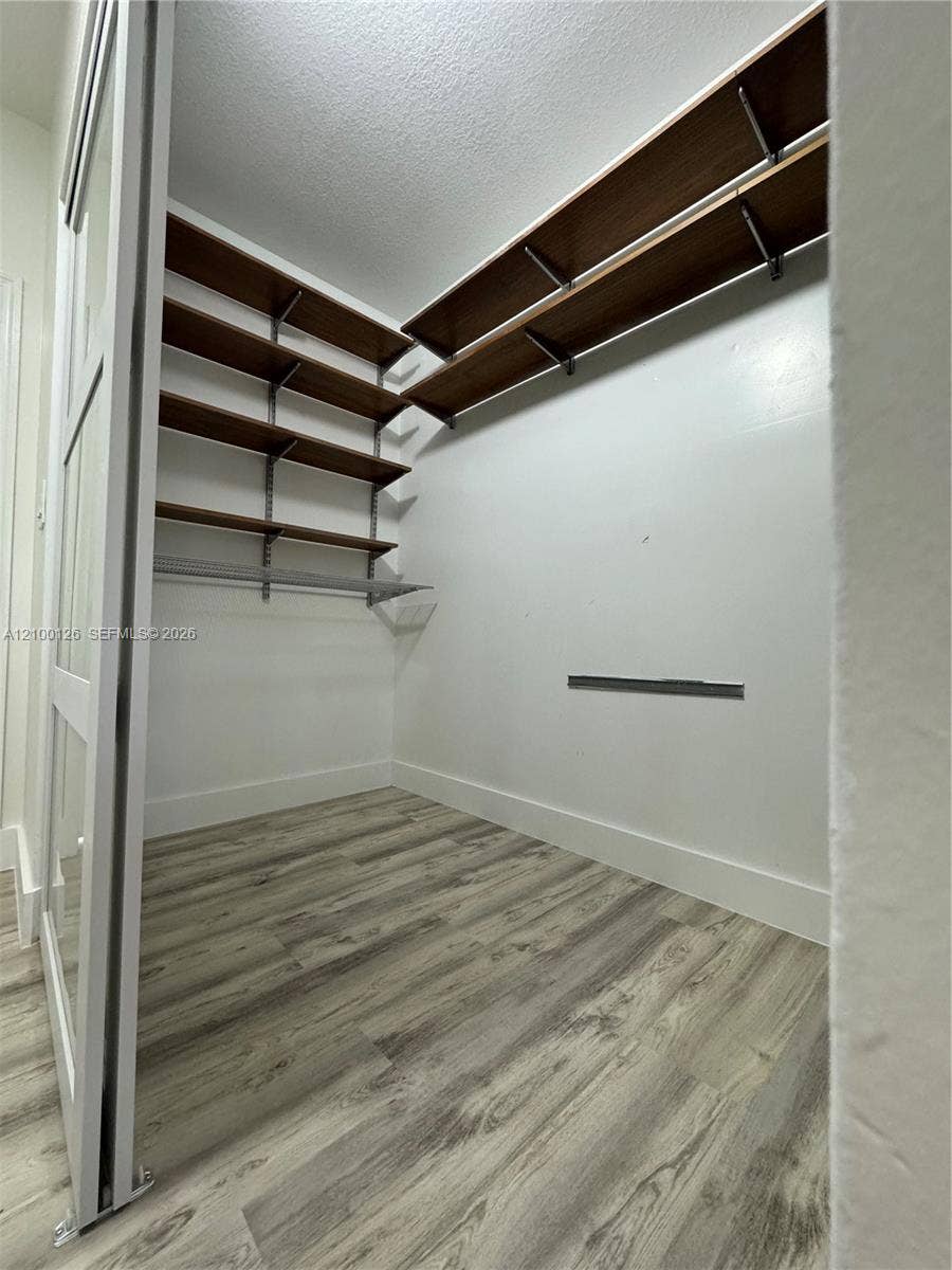 Storage area featuring wood-finish shelving, an adjustable metal track mounting system, wood-finish flooring, and a sliding glass-panel door