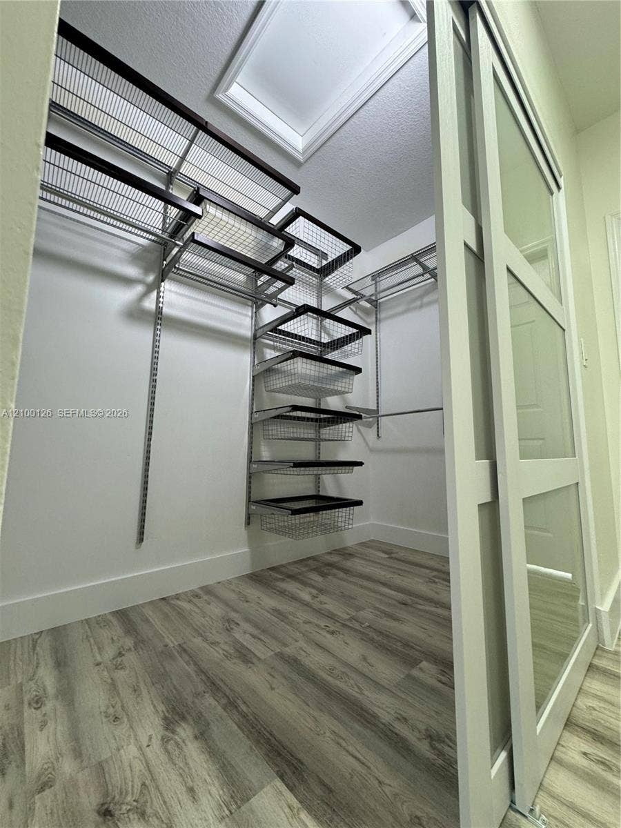 Walk-in closet featuring wood-finish flooring, a white sliding glass-panel door, and a custom wire shelving system with integrated pull-out drawers