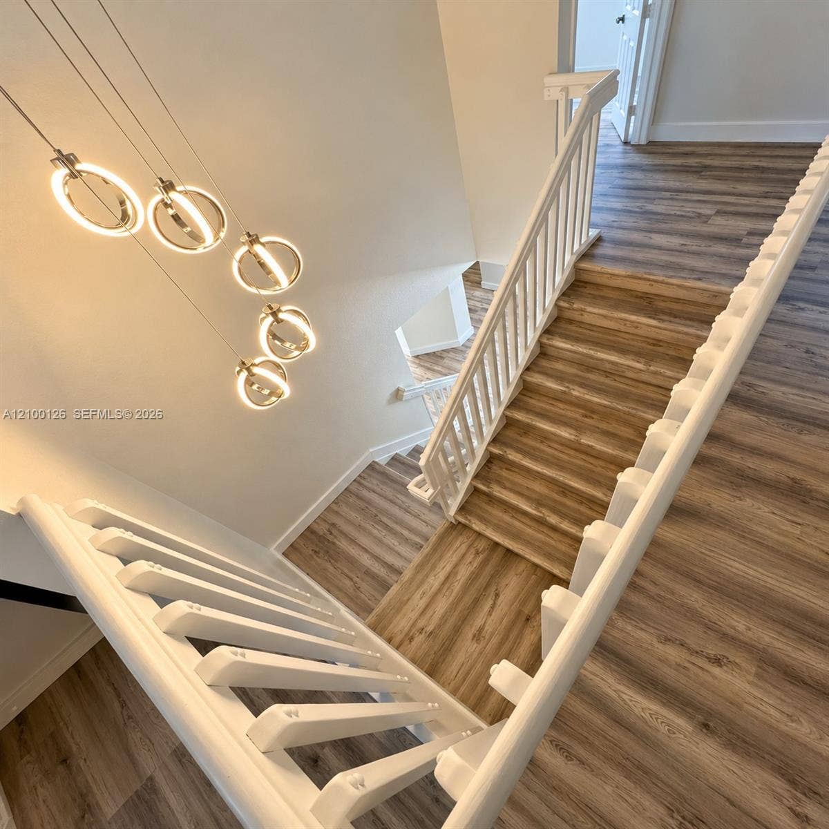 Staircase featuring wood-finish flooring, white railing with vertical balusters, and a tiered circular pendant light fixture