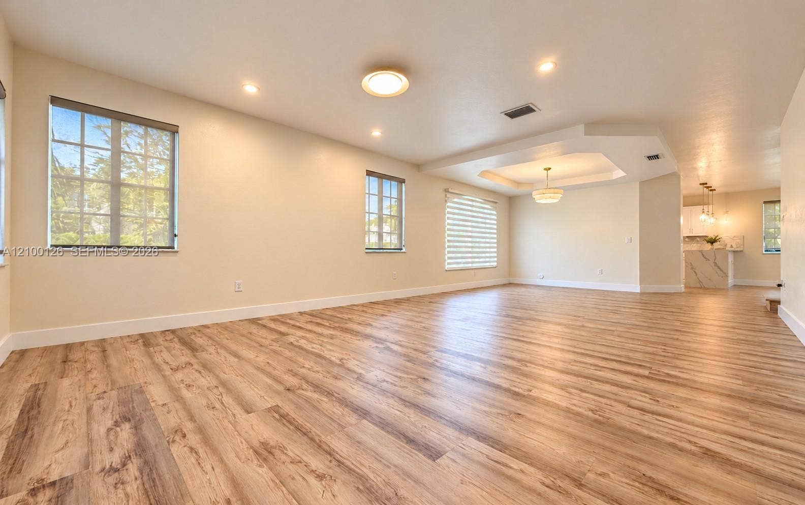 Open-concept interior featuring wood-finish flooring, tray ceiling with recessed lighting, multi-pane windows, and a suspended chandelier