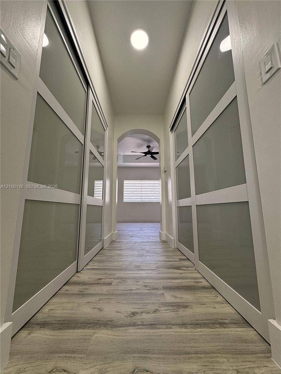 Hallway featuring wood-finish flooring, dual sliding closet doors with frosted glass panels, and an arched architectural opening