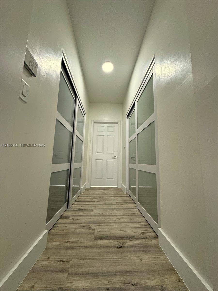 Hallway featuring wood-finish flooring, two sets of sliding closet doors with frosted glass panels, and a paneled interior door with metal hardware