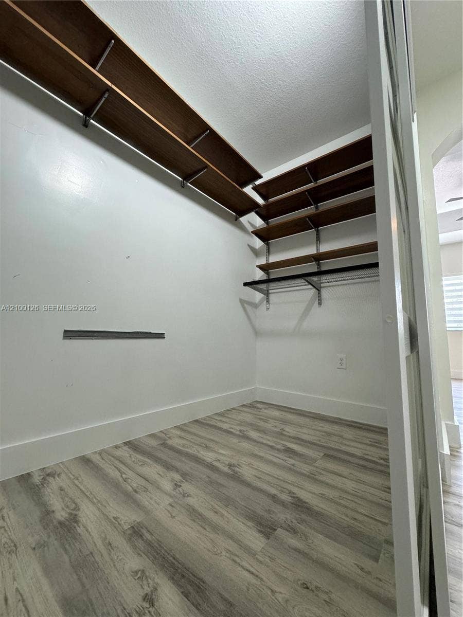 Walk-in closet featuring wood-finish flooring and tiered, built-in shelving with integrated clothing rods