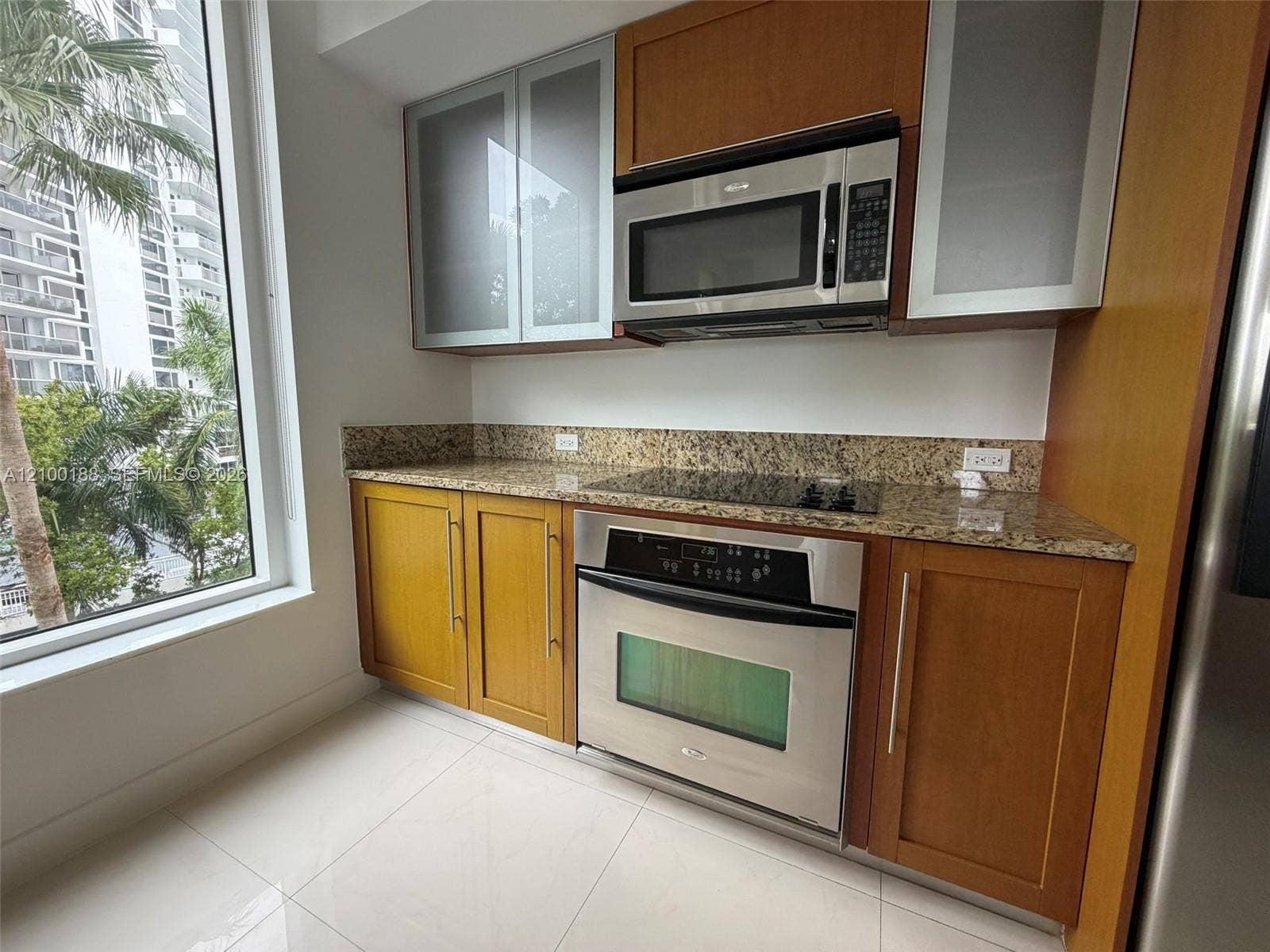 2821 N Ocean Boulevard, #305S, Fort Lauderdale, Fort Lauderdale, FL 33308 Kitchen featuring wood cabinetry, stone countertops, stainless steel built-in appliances, glass-panel upper cabinet doors, and large-format tile flooring