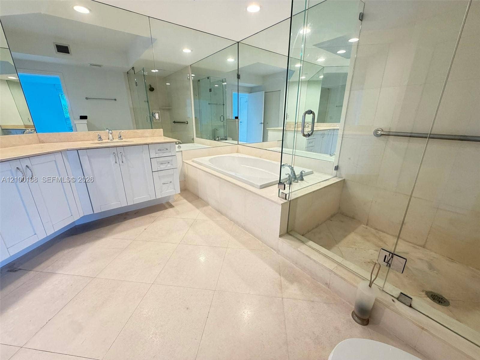 2821 N Ocean Boulevard, #305S, Fort Lauderdale, Fort Lauderdale, FL 33308 Bathroom featuring a double vanity with light-toned countertop, soaking tub with tile surround, glass-enclosed shower, expansive wall-to-wall mirrors, and stone-finish tile flooring