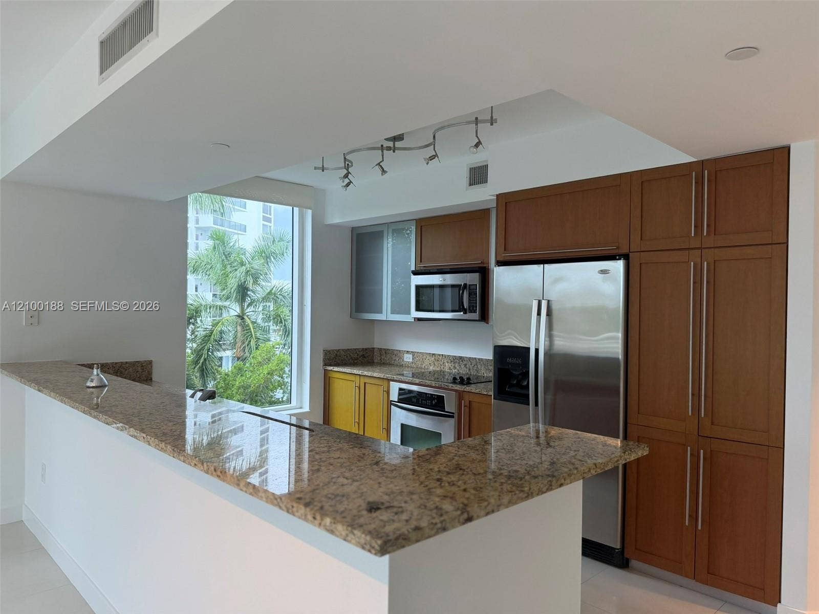 2821 N Ocean Boulevard, #305S, Fort Lauderdale, Fort Lauderdale, FL 33308 Kitchen featuring stone countertops, breakfast bar, built-in cabinetry with glass-panel upper doors, stainless steel appliances, and track lighting