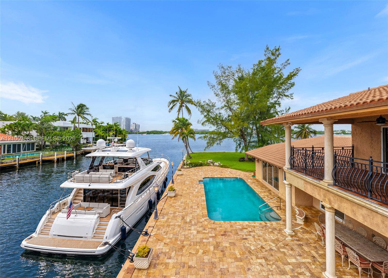 Waterfront estate featuring a private boat slip, rectangular swimming pool, stone-paver patio, covered porch with classical columns, and an upper-level balcony with wrought-iron railings