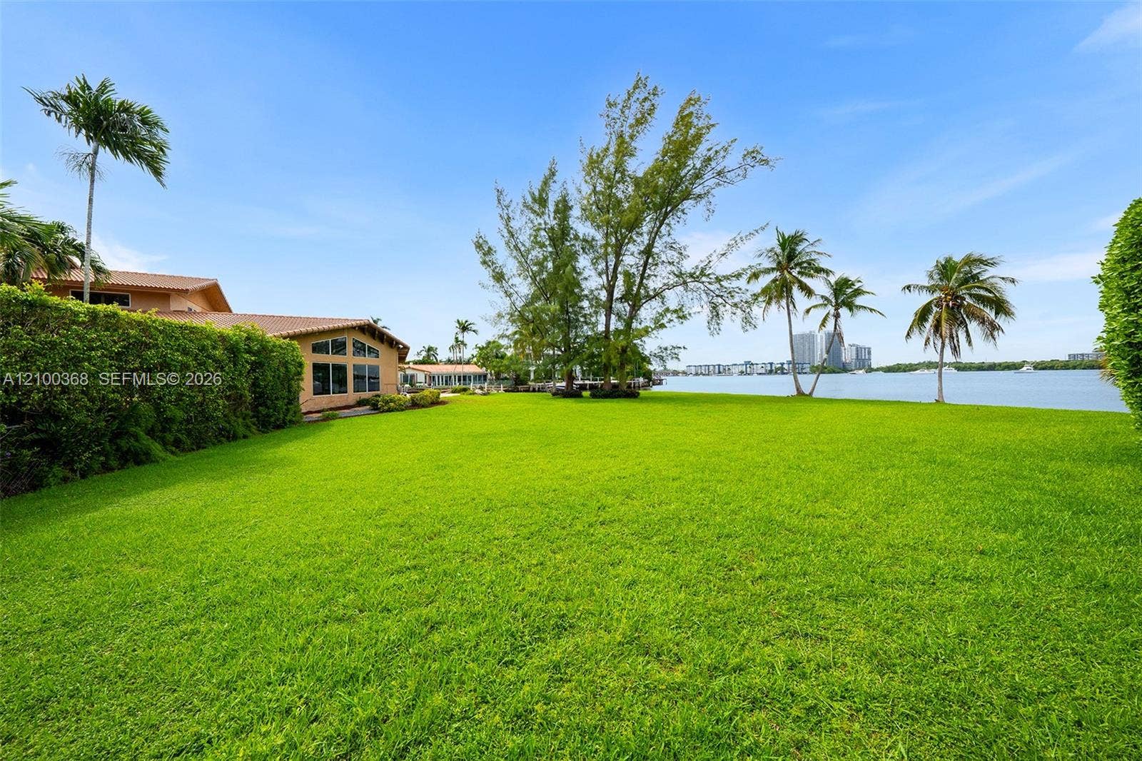 Expansive waterfront lawn featuring manicured turf, mature palm trees, and direct water frontage
