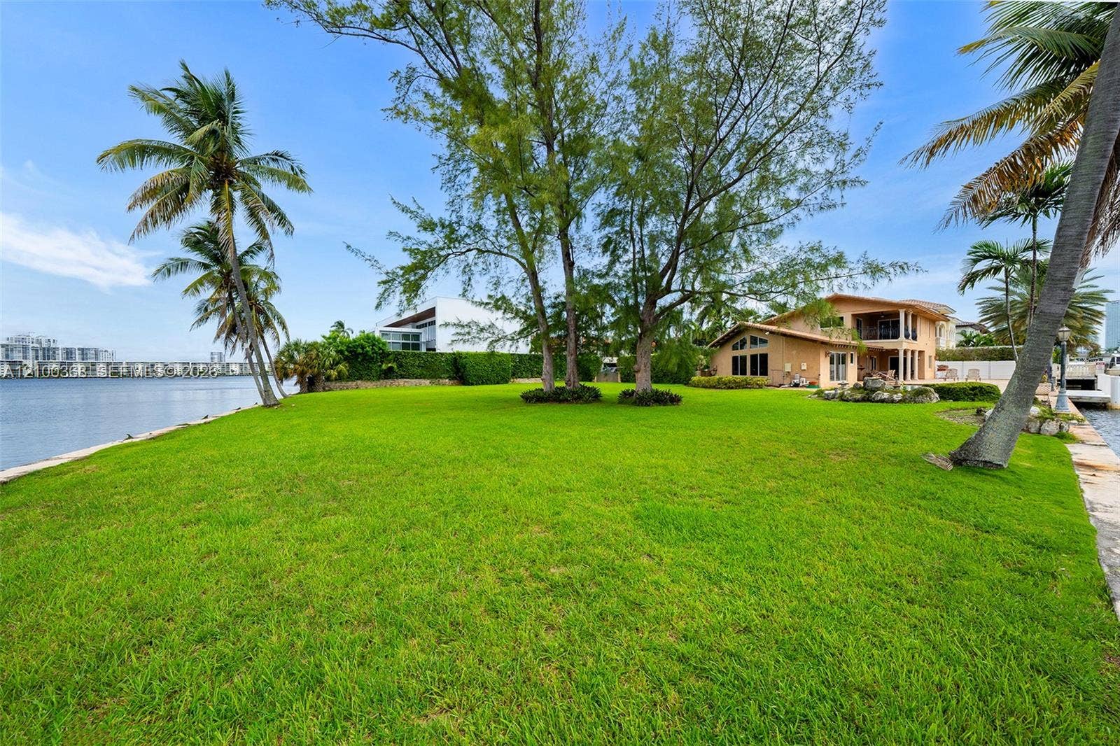 Expansive waterfront property featuring a manicured lawn, mature trees, palm trees, and direct water frontage