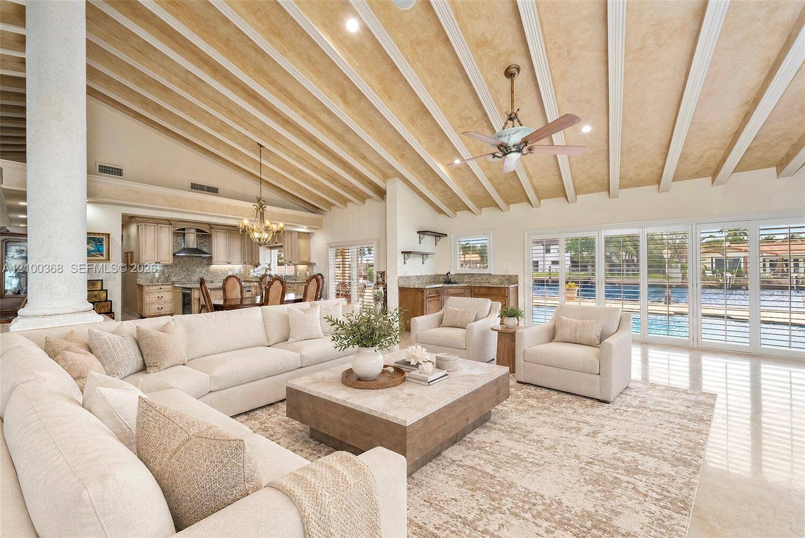 Vaulted ceiling with exposed decorative beams, stone-finish flooring, column architectural detail, built-in wet bar, and multi-panel glass door system