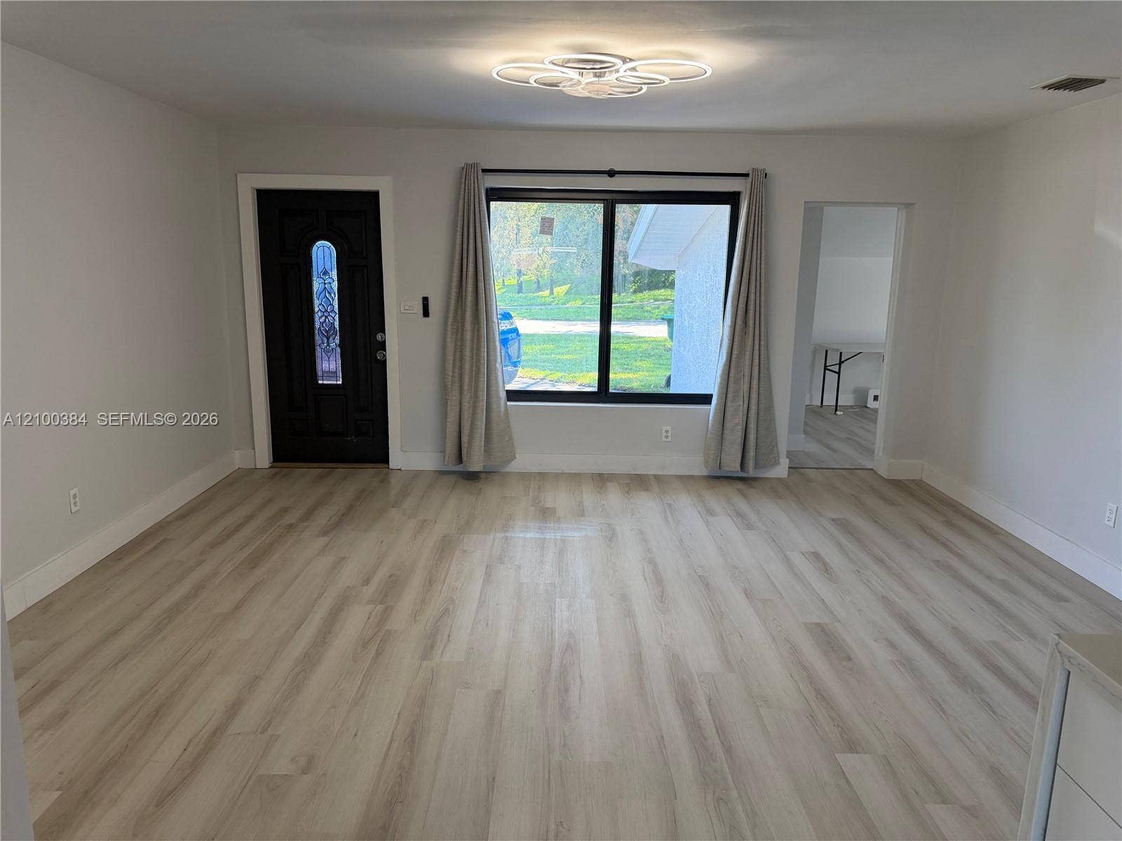 3100 SW 67th Terrace, Miramar, FL 33023 Interior space featuring light-toned wood-finish flooring, a contemporary circular multi-ring flush-mount light fixture, a black-framed window, and a dark-toned exterior entry door with an arched glass insert