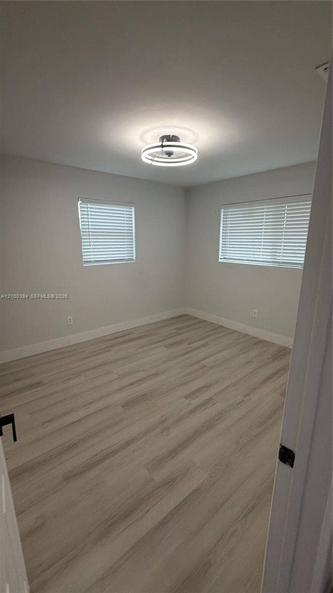 3100 SW 67th Terrace, Miramar, FL 33023 Interior room featuring wood-finish flooring, neutral walls, two windows with horizontal blinds, and a contemporary circular LED ceiling light fixture