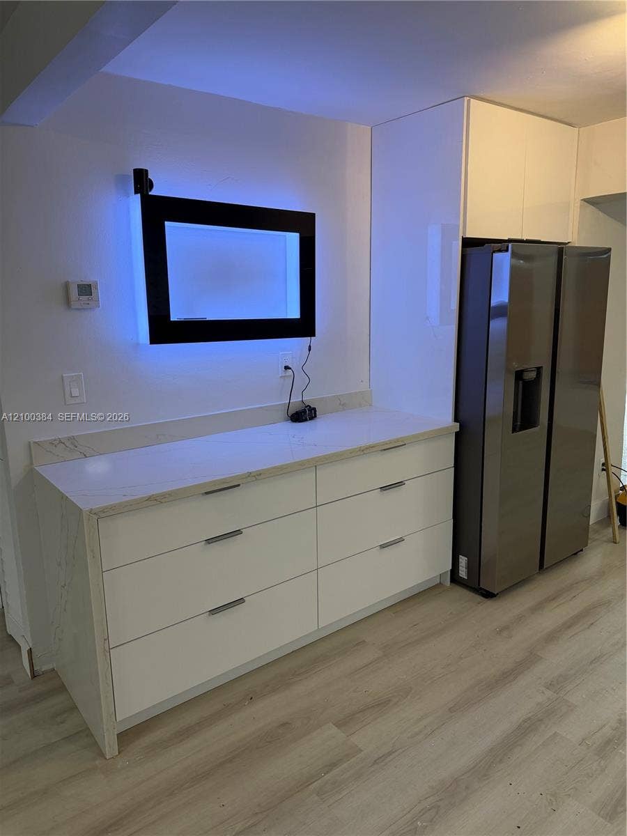 3100 SW 67th Terrace, Miramar, FL 33023 Custom cabinetry featuring white flat-panel drawers, light-toned stone-finish countertops, stainless steel side-by-side refrigerator, and light-tone wood-finish flooring