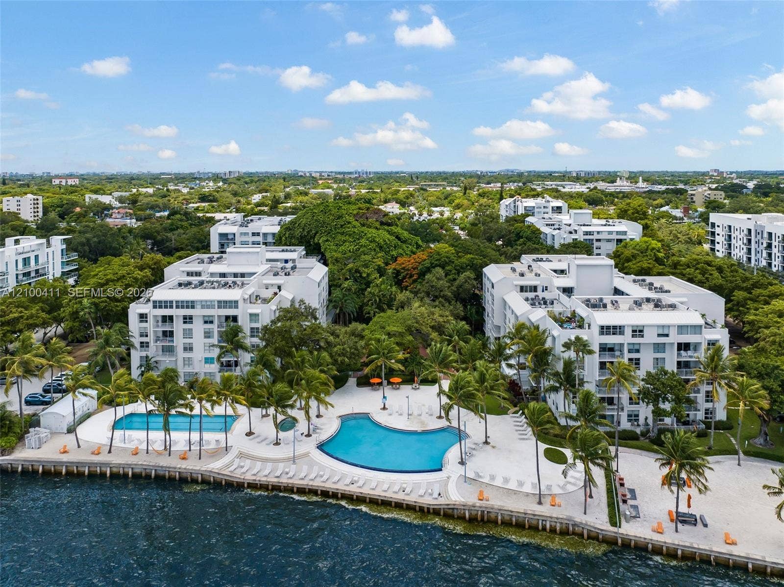 Waterfront condominium complex featuring two outdoor swimming pools, expansive paved sun decks, established tropical landscaping, and bulkhead shoreline protection