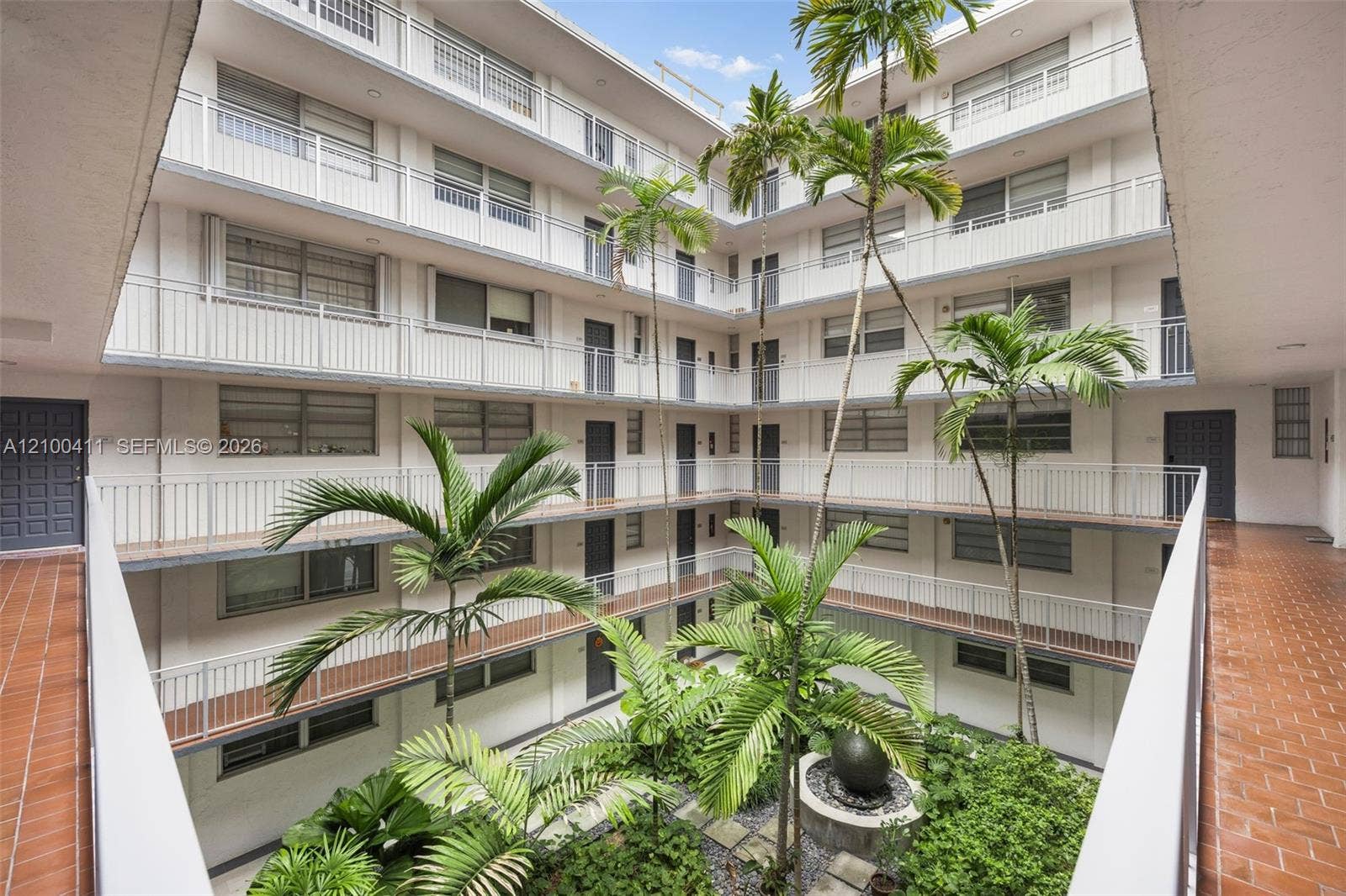 Multi-level open-air central courtyard featuring tile flooring, metal railings, mature palm trees, and a decorative stone fountain