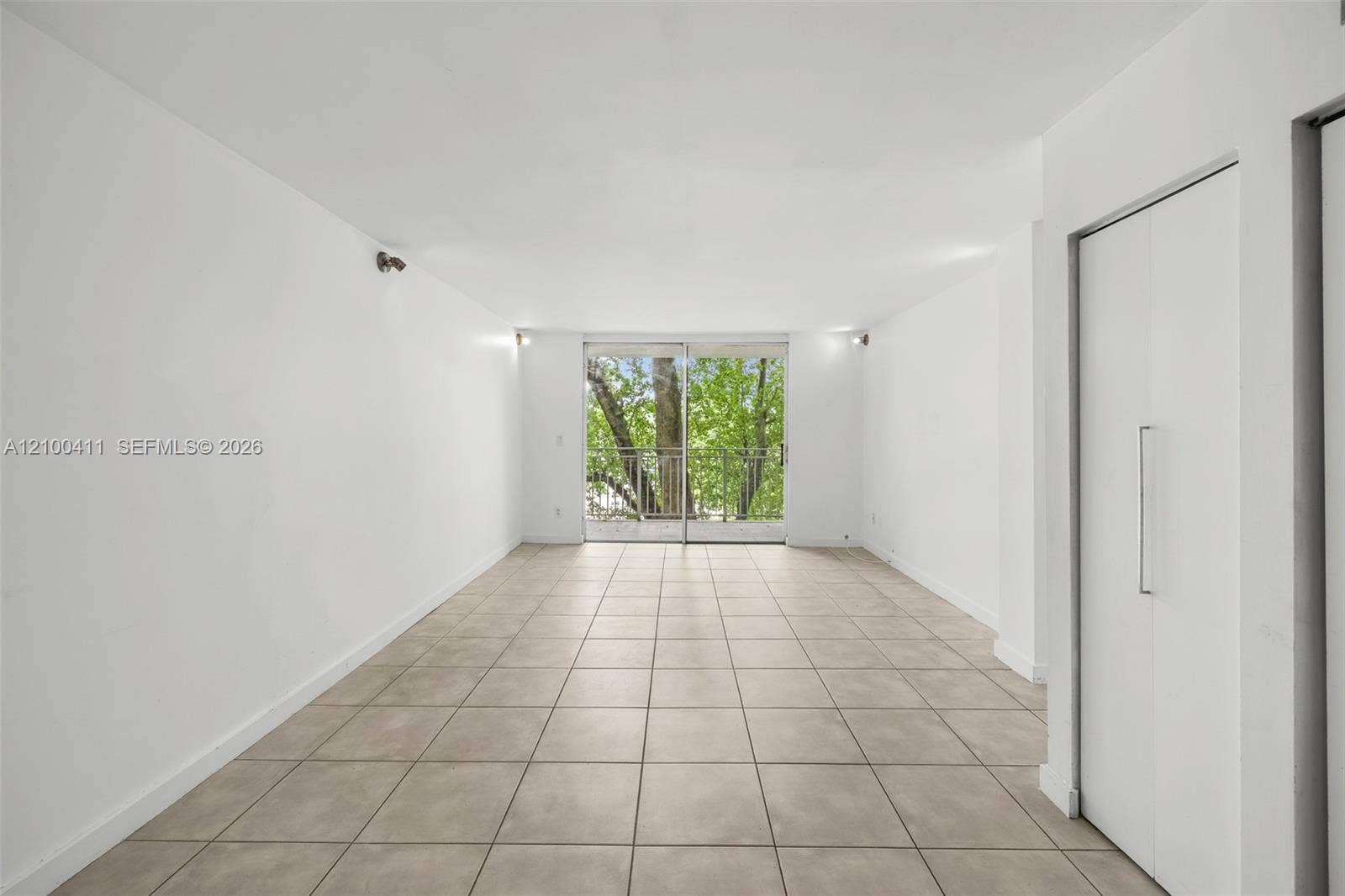 Open-concept space featuring large-format ceramic tile flooring, built-in floor-to-ceiling cabinetry, sliding glass doors, and a metal balcony railing
