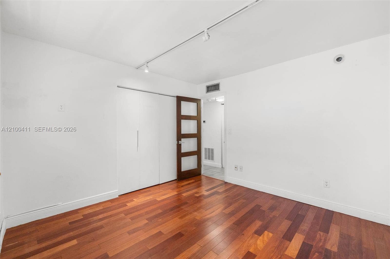 Room featuring wood-finish flooring, white walls, track lighting, built-in sliding closet doors, and a four-panel glass-inset door